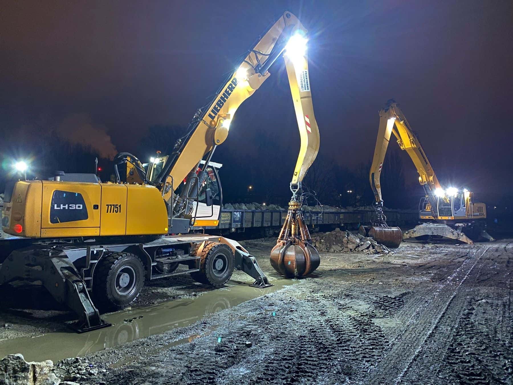 Dwie koparki przeładunkowe Liebherr LH30 pracujące przy torach w świetle halogenów