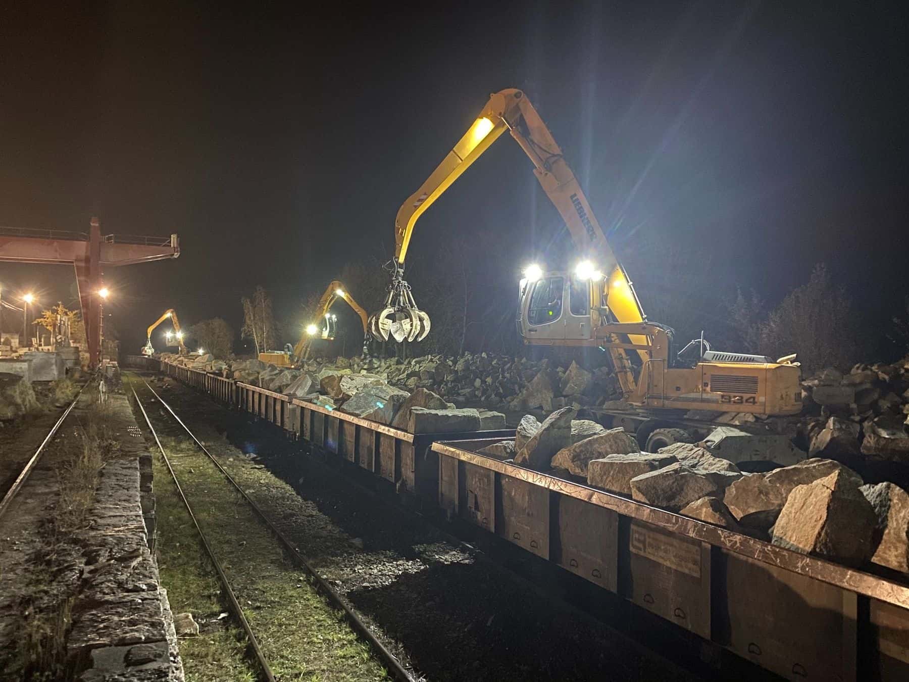Nocny rozładunek składu wagonów z kamieniem, koparka przeładunkowa przy torach