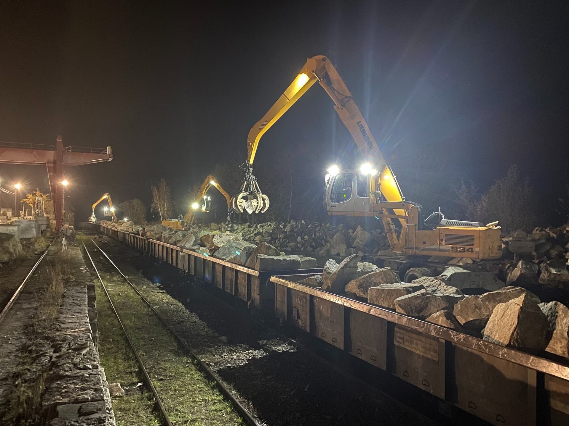 Nocny rozładunek wagonów kolejowych z kamieniem, koparka przeładunkowa Liebherr przy torach