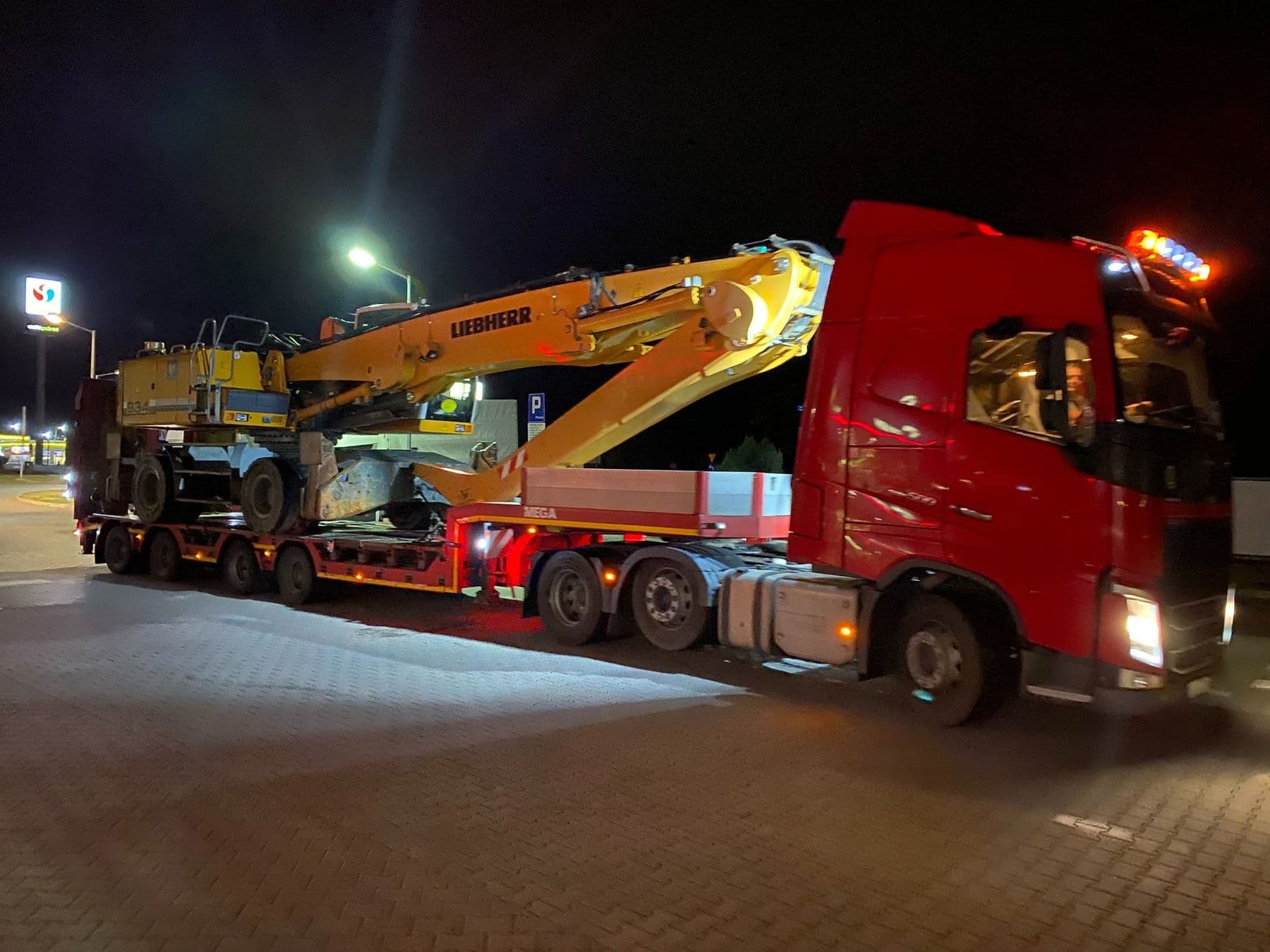 Zestaw niskopodwoziowy z koparką Liebherr na naczepie podczas nocnego przejazdu